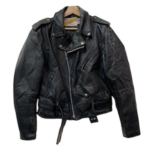 May include: Black leather motorcycle jacket with a classic design. Features a notched collar, asymmetrical zipper, multiple pockets, and a belt at the waist. The jacket shows signs of wear, adding to its vintage appeal.