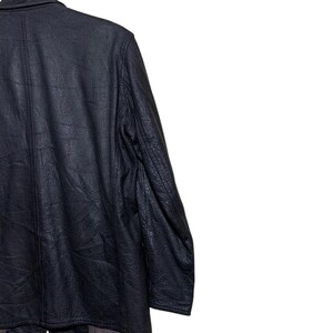 May include: A black leather jacket with a textured finish. The jacket has a classic design with a notched collar and a button closure. The sleeves are long, and the jacket appears to be in good condition. The jacket is hanging on a wooden hanger.