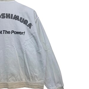May include: White jacket with black text that reads "YOSHIMURA" and "Got The Power!". The jacket has a ribbed hem and cuffs with black stripes. The collar has a black stripe. The jacket is made of a light-colored fabric.