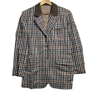 May include: A vintage blazer with a brown suede collar and a plaid pattern in shades of brown, navy, and cream. The jacket has two front pockets and is buttoned up. The blazer is hanging on a wooden hanger.