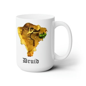 Puede incluir: Taza de cerámica blanca con una imagen marrón y dorada de una piel de ciervo con cuernos, una hoz y una planta verde. La palabra "Druid" está impresa en gris debajo de la imagen.