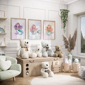 May include: A nursery room with a white dresser and a light green armchair. There are three framed watercolor prints of mermaids on the wall. There are also several stuffed teddy bears on the dresser and a rug on the floor.
