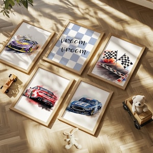 May include: A collection of framed watercolor art prints featuring race cars, checkered flags, and the text "vroom vroom". The prints have a light wood frame and are arranged on a wooden floor. A toy car and a teddy bear in a wooden car are also present.