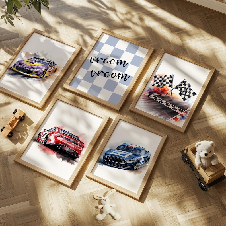 May include: A collection of framed watercolor art prints featuring race cars, checkered flags, and the text "vroom vroom". The prints have a light wood frame and are arranged on a wooden floor. A toy car and a teddy bear in a wooden car are also present.