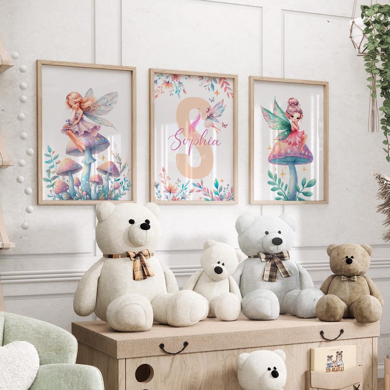 Peut inclure: Trois impressions encadr&eacute;es avec des illustrations &agrave; l'aquarelle de f&eacute;es assises sur des champignons. Les impressions ont une palette de couleurs rose p&acirc;le, bleu et vert. L'impression du milieu pr&eacute;sente le nom "Sophia" en lettres roses. Les impressions sont affich&eacute;es sur un mur au-dessus d'une &eacute;tag&egrave;re en bois avec des animaux en peluche.