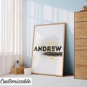 May include: A white framed print with a watercolor background in shades of gray and yellow. The name "ANDREW" is printed in black bold letters with a black tire tread print underneath.