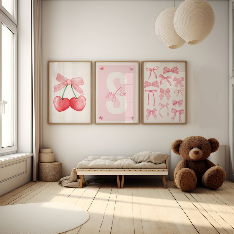 May include: Three pink framed prints on a white wall. The prints feature a pink bow with cherries, the name "Sofia" in pink letters, and a collection of pink bows.