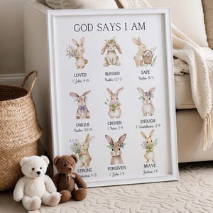 May include: White framed art print with the text "GOD SAYS I AM" and illustrations of bunnies with floral accents. The print includes the words "LOVED", "BLESSED", "SAFE", "UNIQUE", "CHOSEN", "ENOUGH", "STRONG", "FORGIVEN", and "BRAVE".