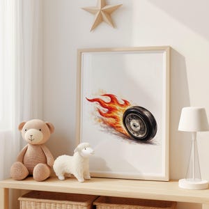 May include: Framed artwork featuring a black tire with flames, set against a white background. The artwork is in a light wooden frame. A teddy bear, a lamb, and a lamp are on a wooden shelf below the artwork.