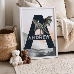 May include: Framed art print featuring a teal dragon over a navy blue letter "A" with the name "ANDREW" in white. The background shows a mountain landscape with a peach and gray color palette. A white frame surrounds the artwork.