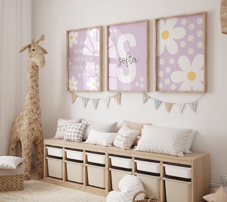 May include: Three framed prints with a purple background and white daisy flowers. The middle print has the name "Sofia" in black cursive writing. The left print has the text "How wonderful life is now you're in the world".