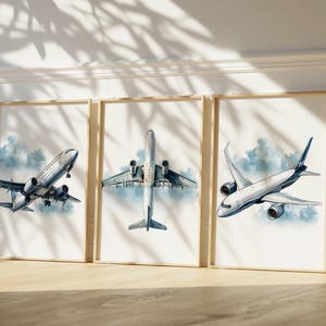 Puede incluir: Tres impresiones art&iacute;sticas enmarcadas con ilustraciones de acuarela de aviones. Cada impresi&oacute;n muestra un dise&ntilde;o de avi&oacute;n diferente, sobre un fondo de suaves nubes azules. Los marcos son de color madera clara, a&ntilde;adiendo un toque natural a la obra de arte con tem&aacute;tica de aviaci&oacute;n.