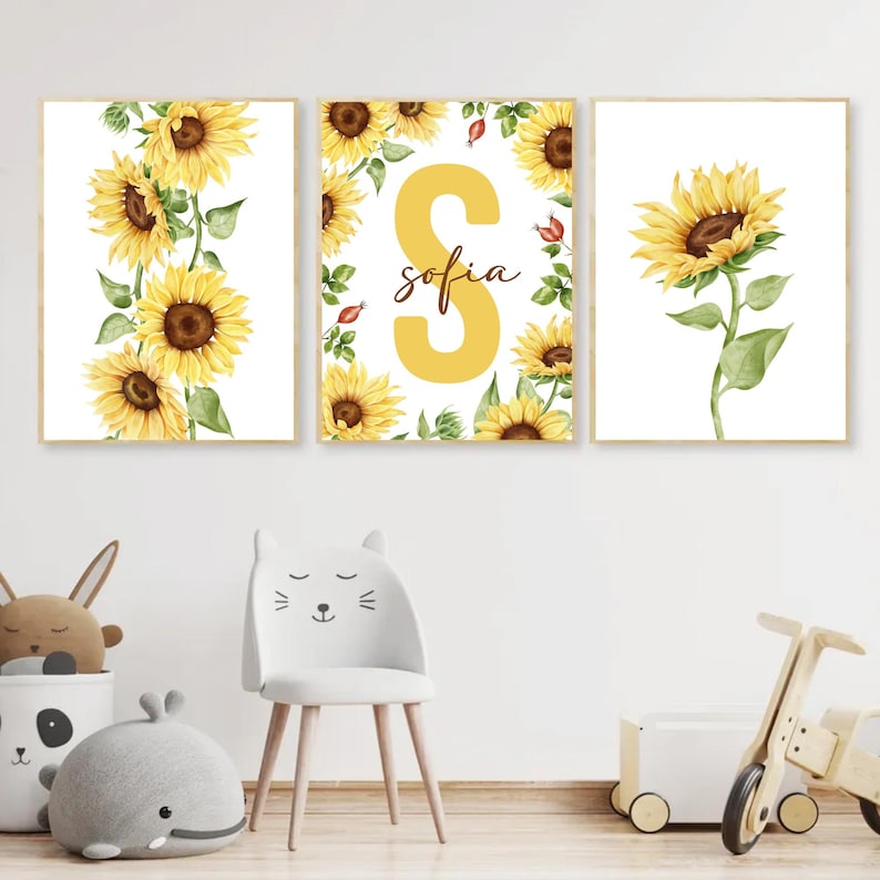 May include: Three watercolor prints featuring sunflowers and the letter "S" with the name "sofia" written below. The prints are framed in a light wood frame.