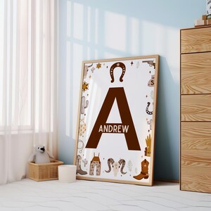 May include: A brown letter A with the name "ANDREW" printed below it. The letter is surrounded by a white border and a variety of western-themed illustrations, including cacti, horseshoes, stars, and cowboy boots.