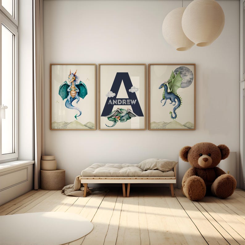 May include: Three framed prints with watercolor illustrations of dragons. The middle print features the letter "A" in a navy blue triangle with the name "ANDREW" written below it. The prints are hanging on a white wall in a child's bedroom.