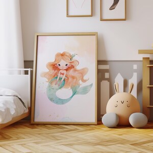 May include: A watercolor illustration of a mermaid with long, flowing blonde hair and a teal tail. The mermaid is sitting on a pink and blue background with gold glitter.