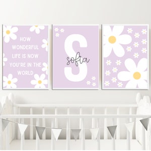 May include: Three purple and white nursery prints with a daisy motif. The first print says "How wonderful life is now you're in the world". The second print has a large white letter "S" with the name "sofia" written in cursive below it. The third print has a large white daisy with a yellow center and smaller white daisies scattered around it.