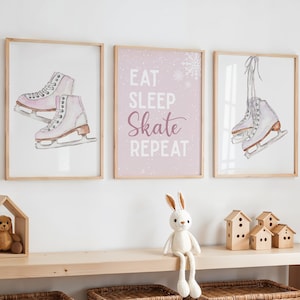 May include: Three framed prints with a winter sports theme. Two prints feature watercolor illustrations of ice skates in pink and white. The centre print has the text "EAT SLEEP SKATE REPEAT" on a pink background.