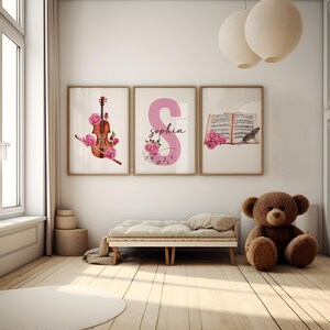 May include: Three framed prints with a watercolor design. The first print features a violin with pink roses, the second print features the letter S in pink with the name "sophia" written below, and the third print features a book with musical notes and a bird with pink roses.