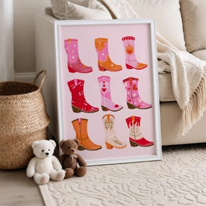 K&ouml;nnte beinhalten: Ein gerahmter Druck mit neun farbenfrohen Cowboy-Stiefeln in verschiedenen Designs und Farben, darunter Rosa, Orange, Rot und Wei&szlig;. Die Stiefel sind mit Sternen, Herzen und Flammen verziert, vor einem zarten rosa Hintergrund.