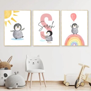 May include: Three watercolor prints featuring a penguin with a yellow sun, a penguin fishing, and a penguin holding a balloon above a rainbow. The middle print has the name "Sarah" written in pink.