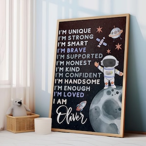 Może przedstawiać: Czarno-biały plakat z motywem kosmicznym. Przedstawia astronautę stojącego na Księżycu, rakietę i gwiazdy. Tekst na plakacie brzmi: "Jestem wyjątkowy, jestem silny, jestem mądry, jestem odważny, jestem wspierany, jestem uczciwy, jestem miły, jestem pewny siebie, jestem przystojny, jestem wystarczający, jestem kochany, jestem Oliver."