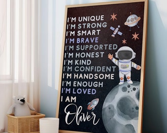 May include: A black and white poster with a space theme. It features an astronaut standing on the moon, a rocket ship, and stars. The text on the poster reads: "I'm unique, I'm strong, I'm smart, I'm brave, I'm supported, I'm honest, I'm kind, I'm confident, I'm handsome, I'm enough, I'm loved, I am Oliver."