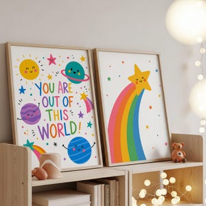 May include: Two framed art prints with a space theme. One features planets, stars, and the text "YOU ARE OUT OF THIS WORLD!". The other shows a smiling star with a rainbow. Both have a white background and wooden frames.