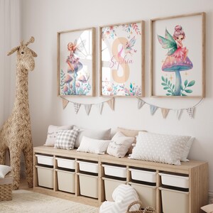 Peut inclure: Trois impressions aquarelle encadr&eacute;es repr&eacute;sentant des f&eacute;es assises sur des champignons. Les impressions sont accroch&eacute;es &agrave; un mur blanc au-dessus d'un banc en bois avec des bacs de rangement. L'impression du milieu porte le nom "Sophia" &eacute;crit en rose.