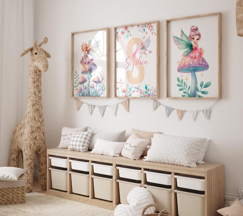 Peut inclure: Trois impressions aquarelle encadr&eacute;es repr&eacute;sentant des f&eacute;es assises sur des champignons. Les impressions sont accroch&eacute;es &agrave; un mur blanc au-dessus d'un banc en bois avec des bacs de rangement. L'impression du milieu porte le nom "Sophia" &eacute;crit en rose.