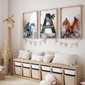 May include: Three framed dragon art prints in a child's room. The prints feature a blue, green, and red dragon. The middle print has the name "Andrew" on it. A woven giraffe and storage bench with pillows and bins are in the room.