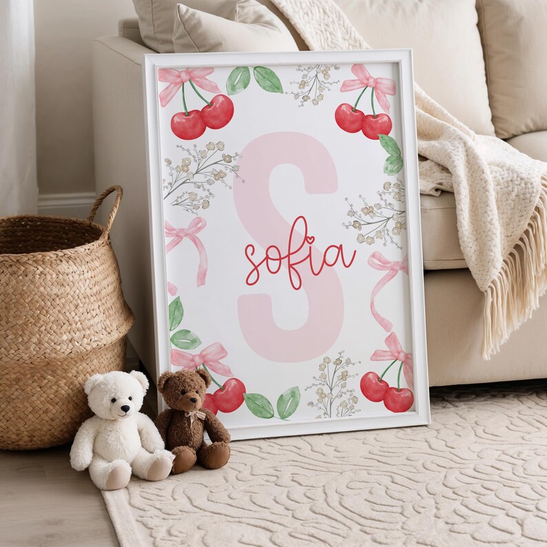 May include: A white framed print with a pink letter S and the name "sofia" written in red cursive. The print is surrounded by a border of green leaves, pink bows, and red cherries.