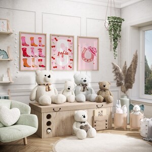 K&ouml;nnte beinhalten: Ein Kinderzimmer mit gerahmten rosa Wandbildern mit Cowboy-Stiefeln, der Zahl 8 mit dem Namen "Sofia" und einem Hufeisen mit einem Herz. Mehrere Teddyb&auml;ren unterschiedlicher Gr&ouml;&szlig;e sitzen auf einer Holzkiste. Ein hellgr&uuml;ner Sessel und dekorative Gegenst&auml;nde vervollst&auml;ndigen die Szene.