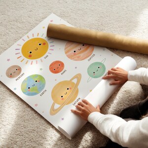 May include: A colorful educational poster featuring the planets of the solar system with smiling faces. The poster includes the sun, Mercury, Earth, Mars, Jupiter, Venus, and Saturn. A rolled-up poster and a brown tube are also visible.