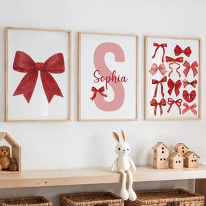 May include: Three framed art prints featuring red bows and the name "Sophia". The first print displays a large red bow. The second print shows the letter "S" in pink with the name "Sophia". The third print showcases various red bow designs.