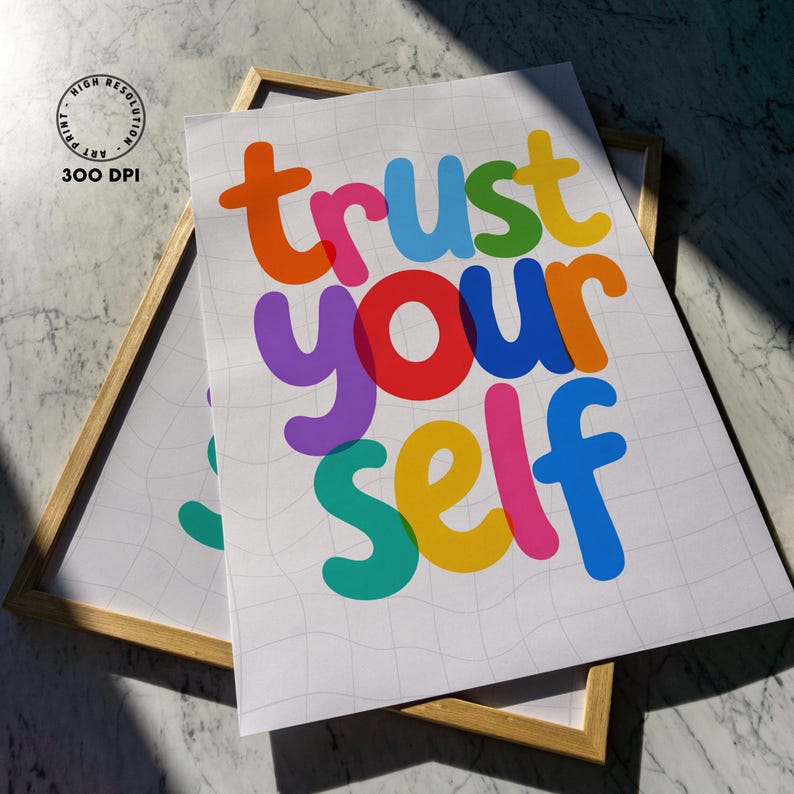 May include: Two framed art prints with the words "trust yourself" in colorful bubble letters. The prints are on a white background with a subtle grid pattern. The frames are a light wood color.