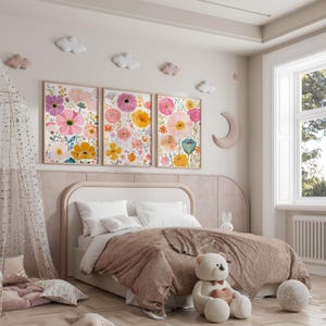 May include: Three framed floral art prints with pink, yellow, and purple flowers hang above a bed with a brown comforter. Decorative clouds and a crescent moon adorn the wall. A teddy bear sits on the floor.