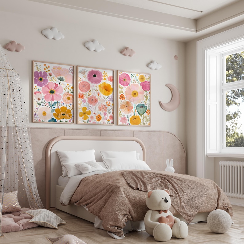 May include: Three framed floral art prints with pink, yellow, and purple flowers hang above a bed with a brown comforter. Decorative clouds and a crescent moon adorn the wall. A teddy bear sits on the floor.