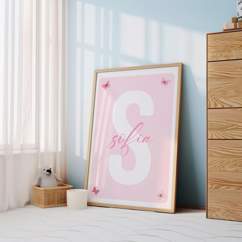May include: A pink and white framed print with the letter "S" and the name "sofia" written in cursive. The print is decorated with pink butterflies.