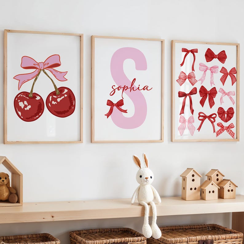 May include: Three framed prints with a pink and red color scheme. The first print features two red cherries with pink bows. The second print features a large pink letter S with the name "Sophia" written in red. The third print features a collection of red and pink bows.