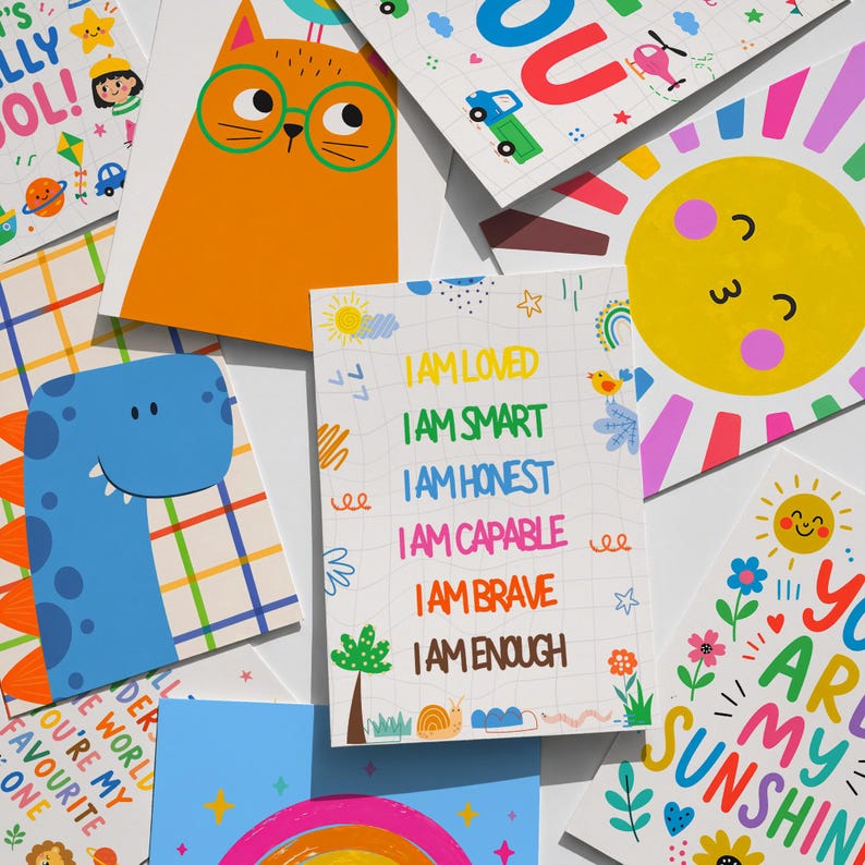May include: A collection of colorful, illustrated cards with positive affirmations and cheerful designs. The cards feature images of a cat, dinosaur, sun, and rainbow, with phrases like "I am loved" and "You are my sunshine."