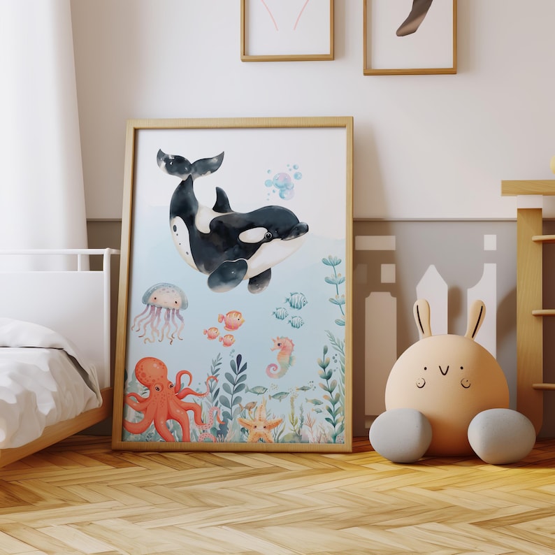 May include: A framed watercolour print depicting an orca whale, jellyfish, octopus, seahorse, and fish. The artwork has a light blue background with aquatic plants and a starfish. The frame is a light wood colour.