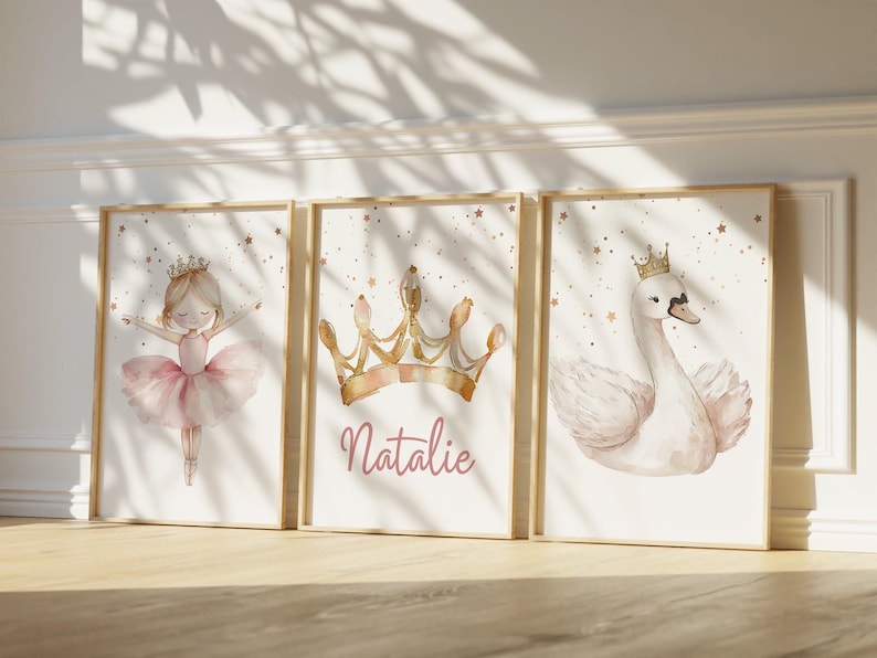 May include: Three framed watercolor prints featuring a ballerina, a crown with the name "Natalie", and a swan wearing a crown. The prints have a soft, pastel color palette with gold star accents, and are set in wooden frames.