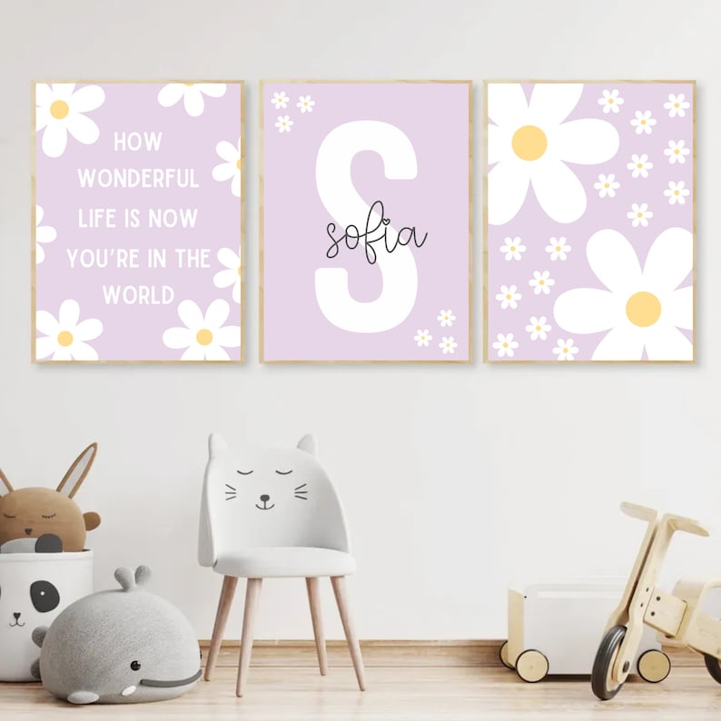 May include: Three framed prints with a light purple background and white daisy flowers. The center print features a large white letter "S" with the name "sofia" written in black cursive. The left print has the text "How wonderful life is now you're in the world". The right print has a large white daisy flower with a yellow center.