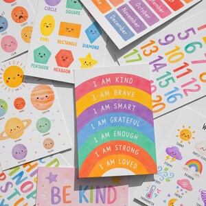 May include: A collection of colorful educational cards with illustrations and text. Cards feature shapes, numbers, planets, months, and positive affirmations like "I am kind." The cards have a cheerful, hand-drawn style, perfect for learning.