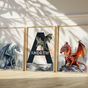 May include: Three framed art prints featuring dragons. One print shows a blue dragon, another has a red dragon, and the center print displays the name "ANDREW" with a green dragon. The prints have a watercolor style.