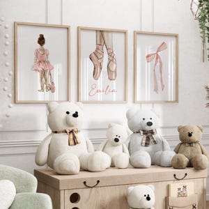 May include: Three framed watercolor prints with a ballerina theme. The prints feature a ballerina in a pink tutu, a pair of pink ballet shoes, and a pink ribbon. The prints are hung on a white wall above a shelf with stuffed teddy bears.