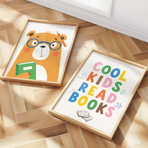 May include: Two framed art prints on a wooden floor. One features a cartoon bear wearing glasses and holding a book. The other print says "COOL KIDS READ BOOKS" in colorful letters, with an illustration of an open book.