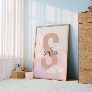 Pu&ograve; includere: Una stampa incorniciata con uno sfondo rosa e pesca che presenta una grande lettera marrone "S" con il nome "sofia" scritto in corsivo sotto. La stampa &egrave; decorata con stelle dorate e nuvole bianche.
