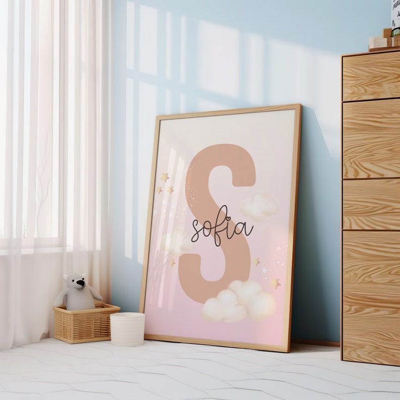 Pu&ograve; includere: Una stampa incorniciata con uno sfondo rosa e pesca che presenta una grande lettera marrone "S" con il nome "sofia" scritto in corsivo sotto. La stampa &egrave; decorata con stelle dorate e nuvole bianche.